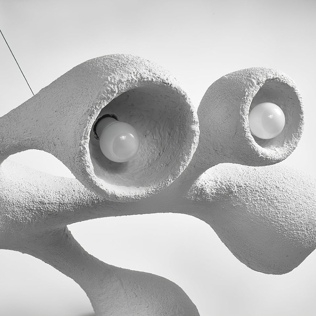 Close view of two bulbs sitting inside the openings of this Clérachic pendant, with the uneven plaster-like white surface around them.