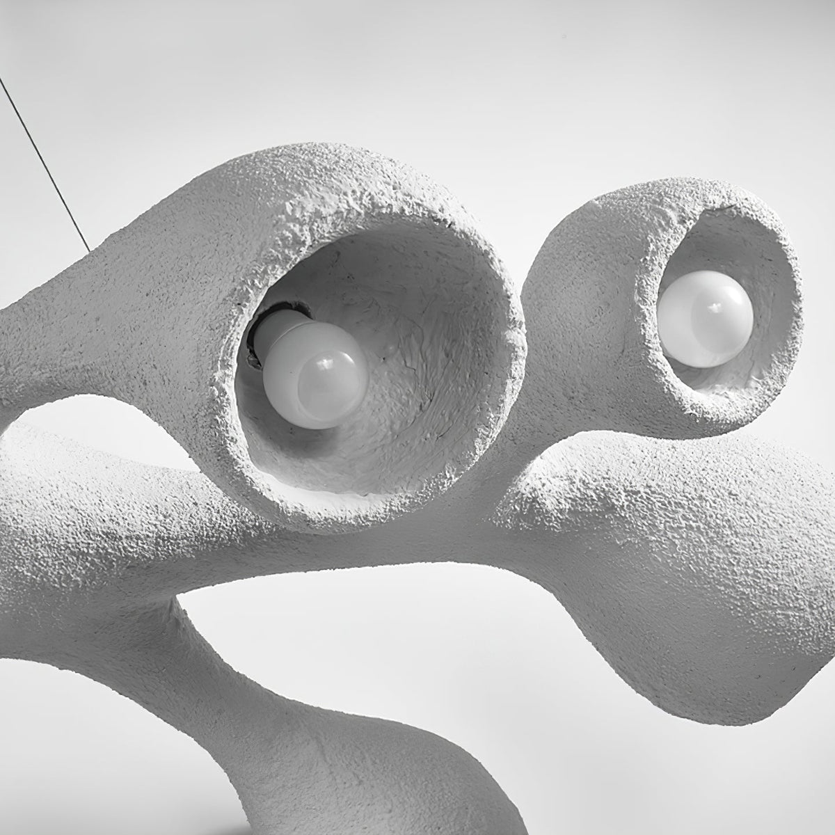 Close view of two bulbs sitting inside the openings of this Clérachic pendant, with the uneven plaster-like white surface around them.