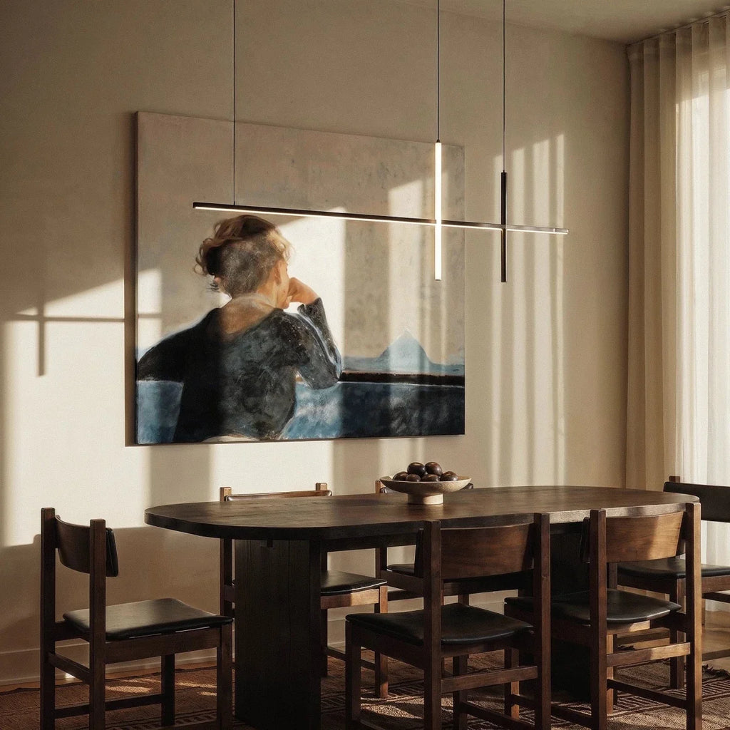 Clérachic pendant light in black hung over a dark wood dining table beside a framed portrait painting.