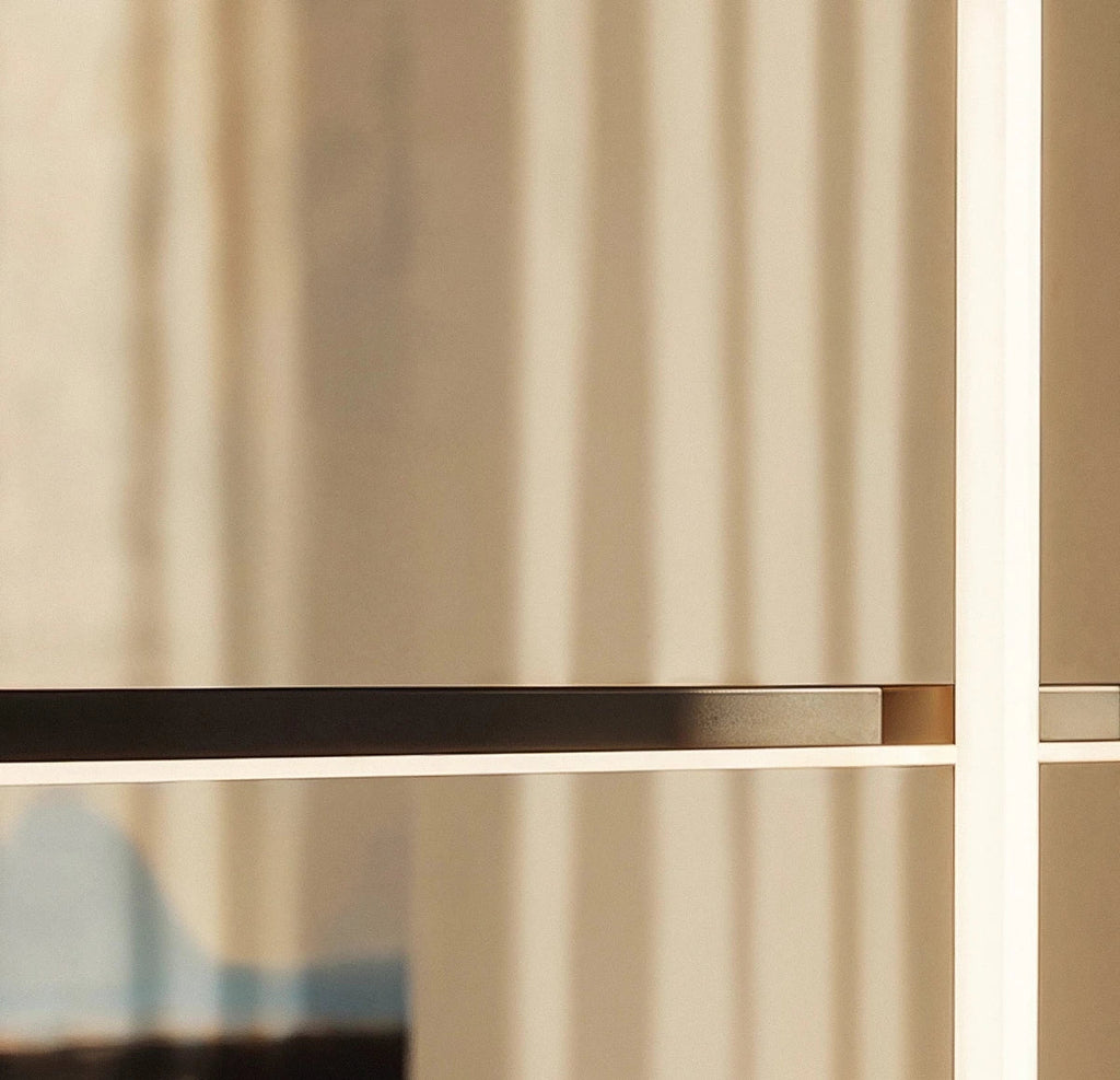 Close-up of the Clérachic pendant light's black horizontal bar crossing a glowing vertical rod, backlit by sheer curtains.
