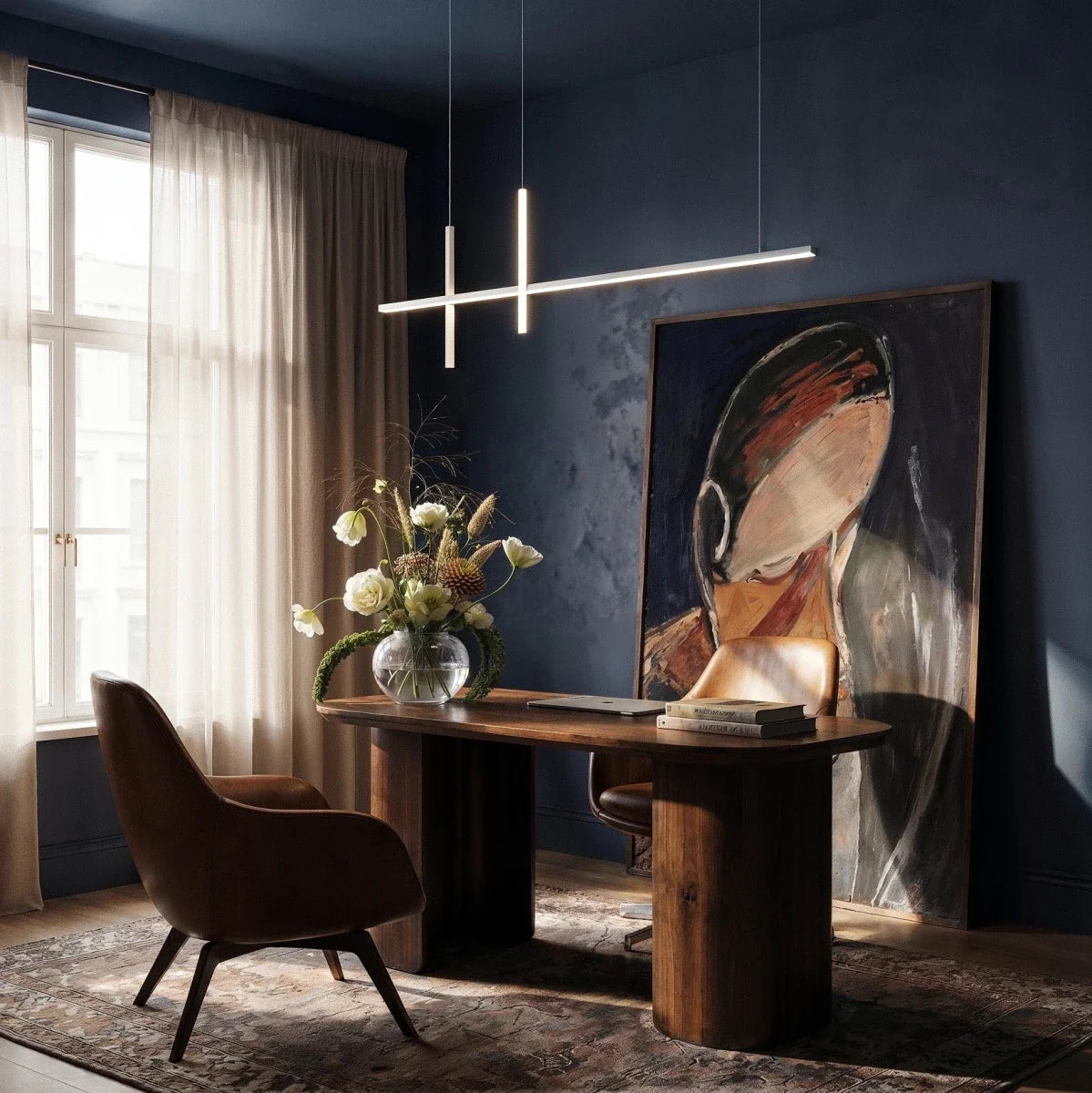 Clérachic pendant light in black suspended over a wooden desk in a dark blue home office with a portrait painting.