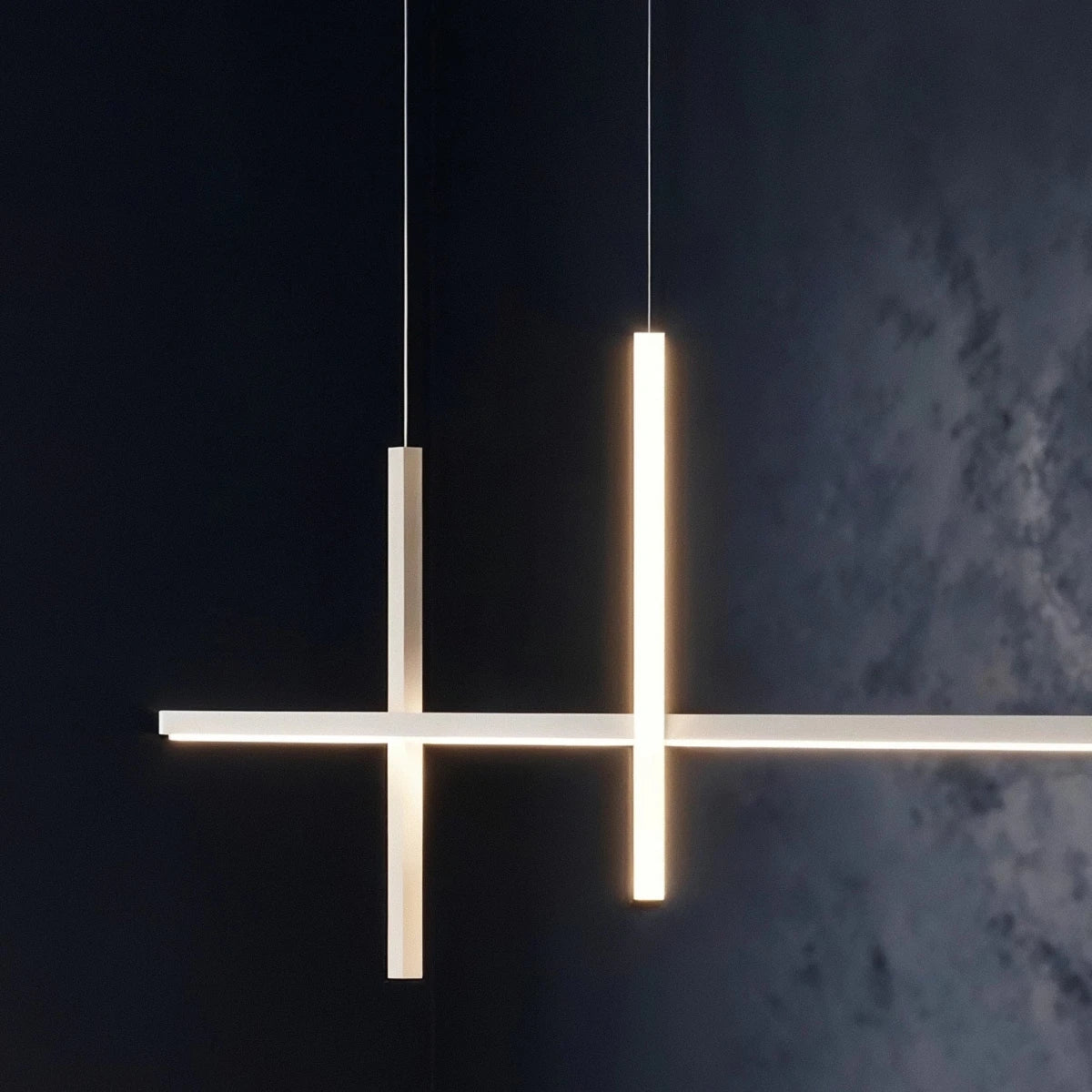 Close-up of the Clérachic pendant light in white, both vertical bars glowing warm against a dark textured wall.