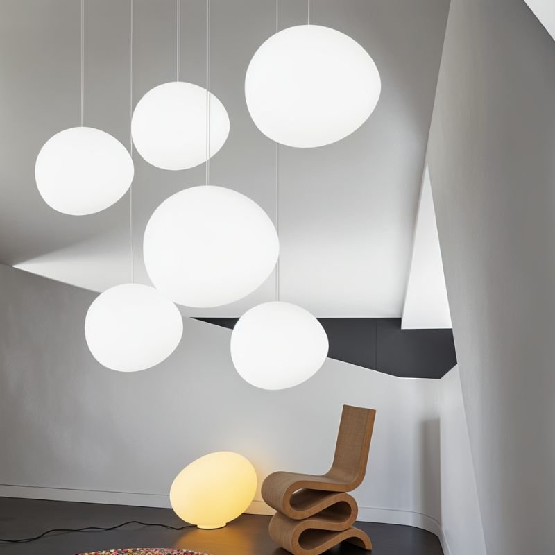 Clérachic group of six white pebble pendants at different heights above a chair and a glowing floor lamp