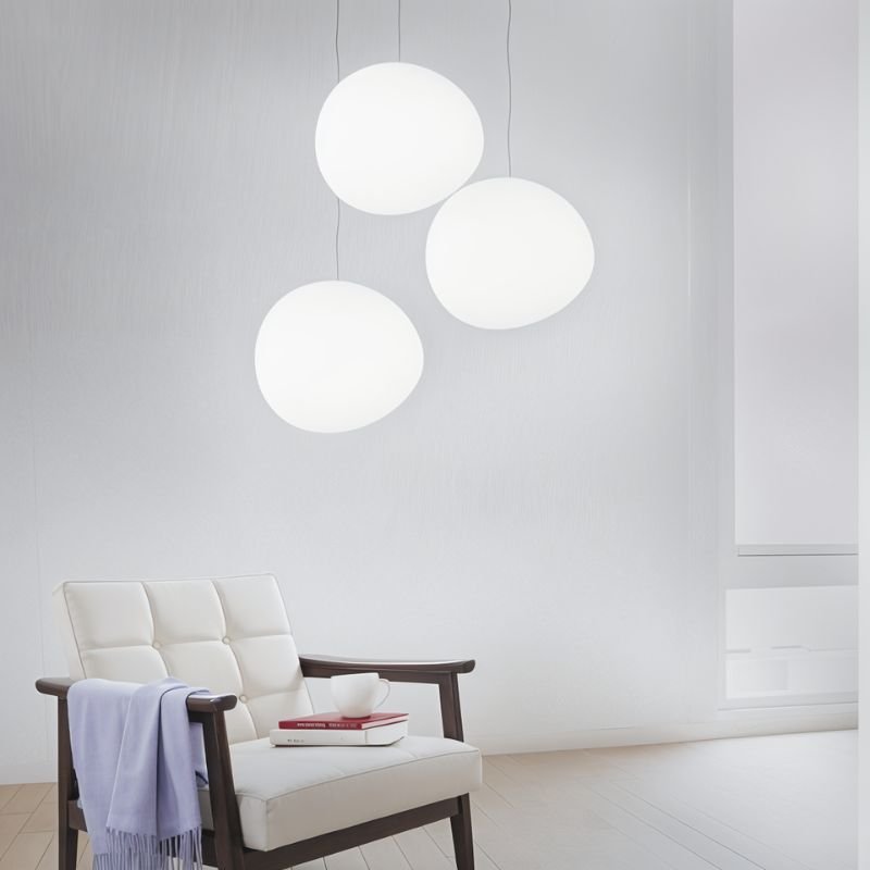 Clérachic trio of white pebble pendants hung at different heights above a cream leather armchair with a throw
