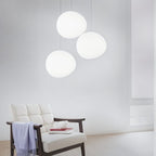 Clérachic trio of white pebble pendants hung at different heights above a cream leather armchair with a throw