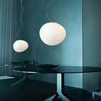 Clérachic two white pebble pendants in different sizes over a dark glass dining table against teal walls