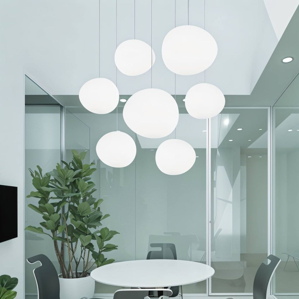 Clérachic cluster of seven white pebble pendants hung at varied heights in a bright meeting room with a plant
