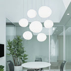 Clérachic cluster of seven white pebble pendants hung at varied heights in a bright meeting room with a plant