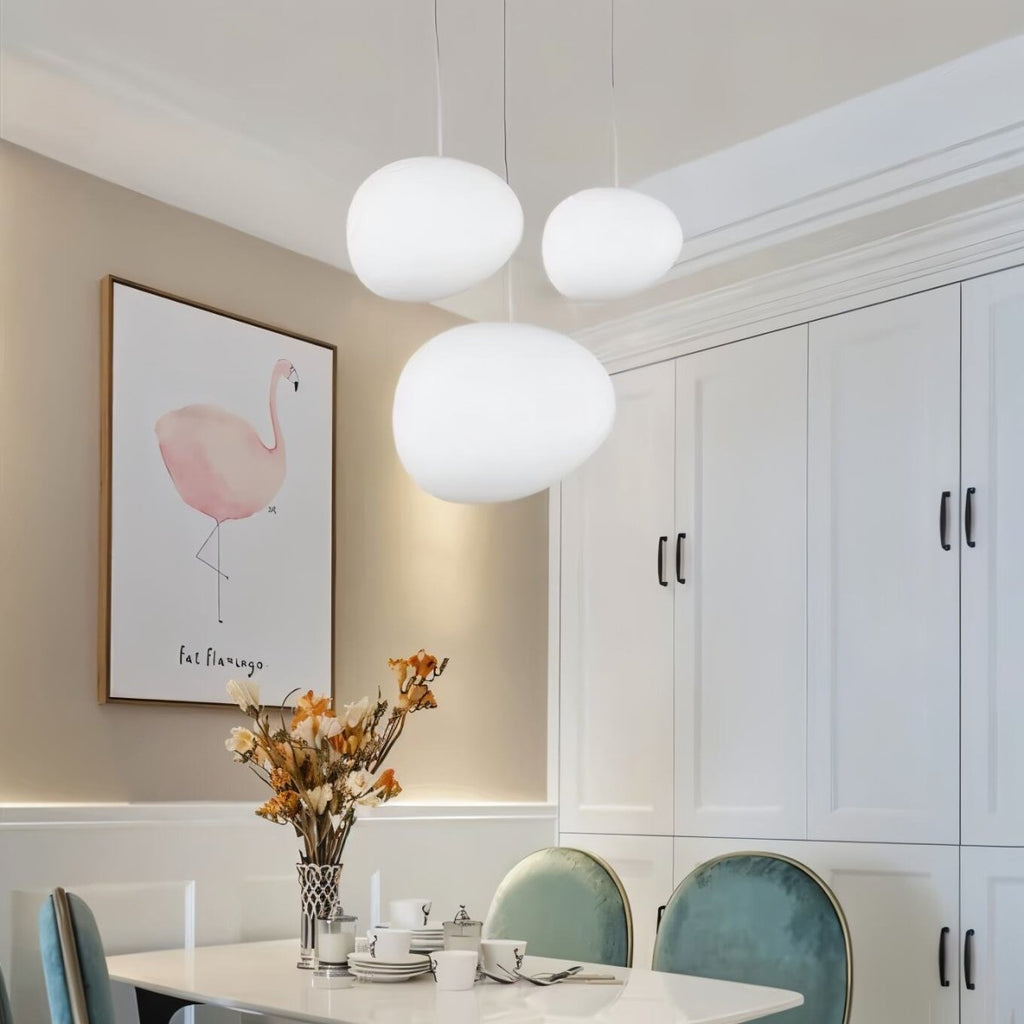 Clérachic three white pebble pendants over a dining table, beside a framed flamingo print and green velvet chairs