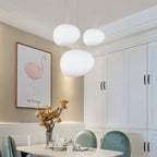 Clérachic three white pebble pendants over a dining table, beside a framed flamingo print and green velvet chairs