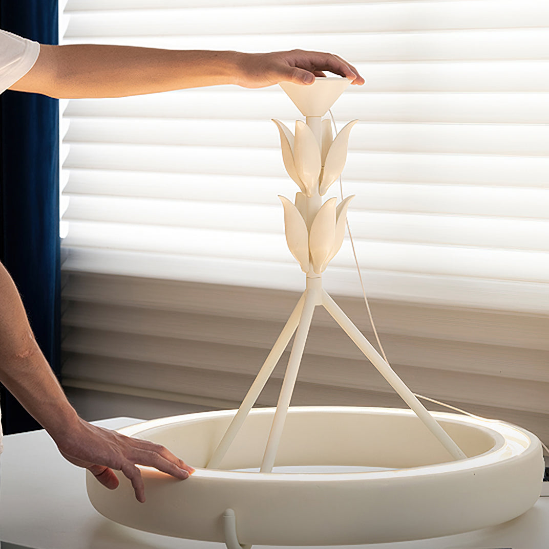A hand steadies the leaf-wrapped stem of this Clérachic ceiling light while it rests on a table in front of window blinds.