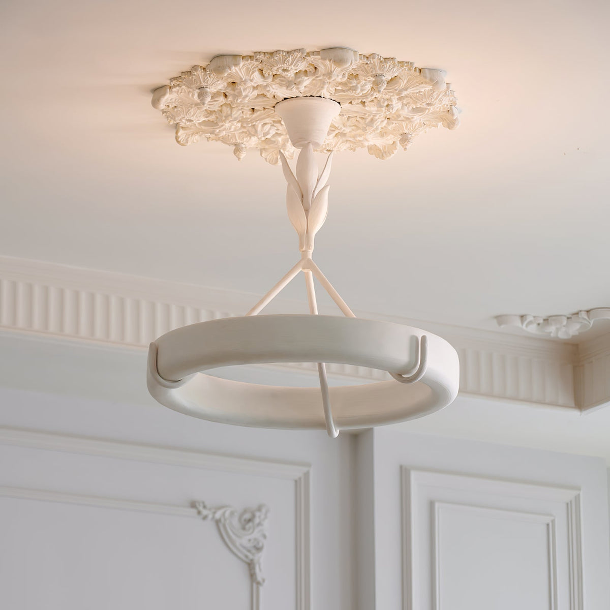 This Clérachic ceiling light hangs from a floral plaster rose, with panelled white walls and moulded cornices behind.
