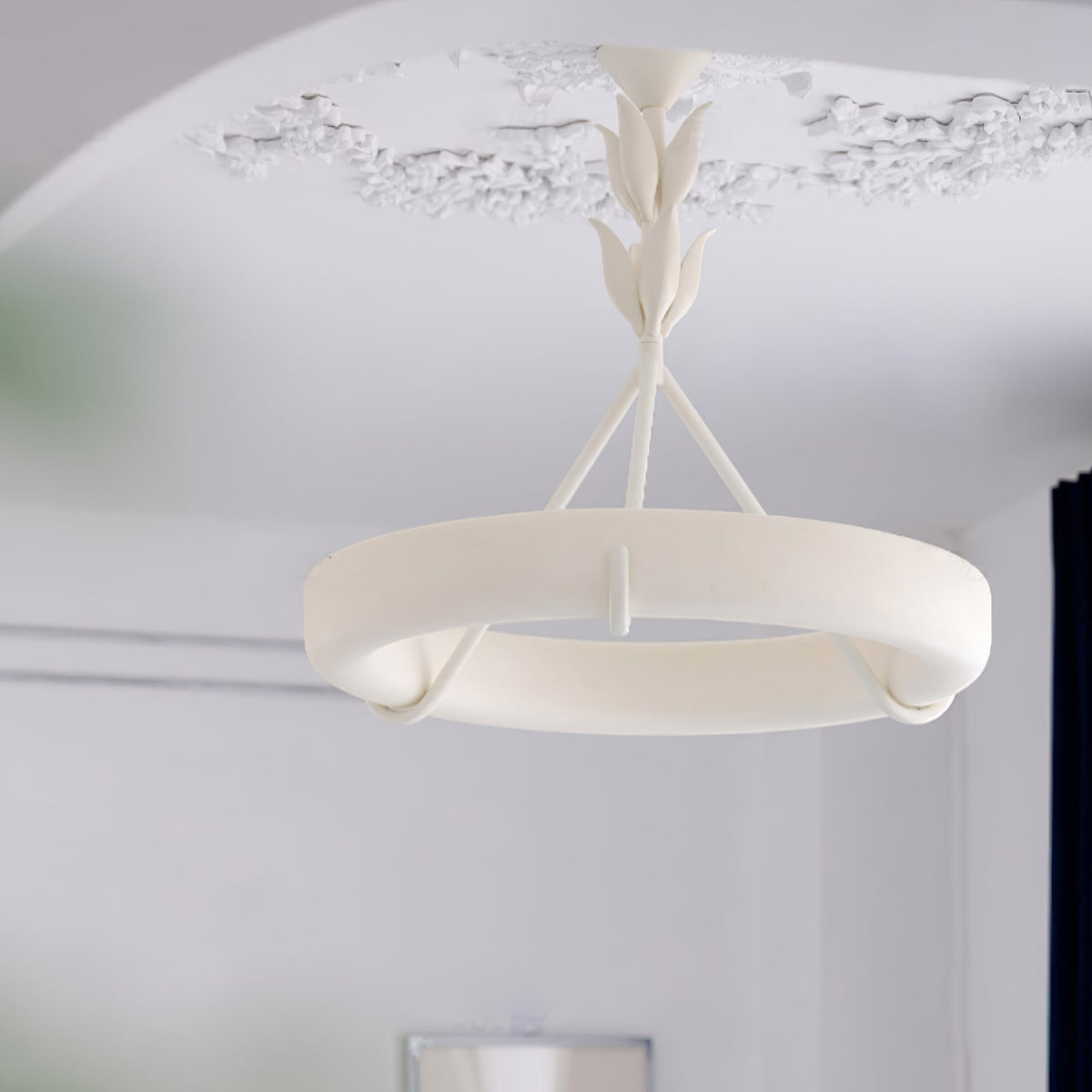 Low view of the white plaster ring of this Clérachic ceiling light, with a detailed ceiling rose above and a plain wall below.