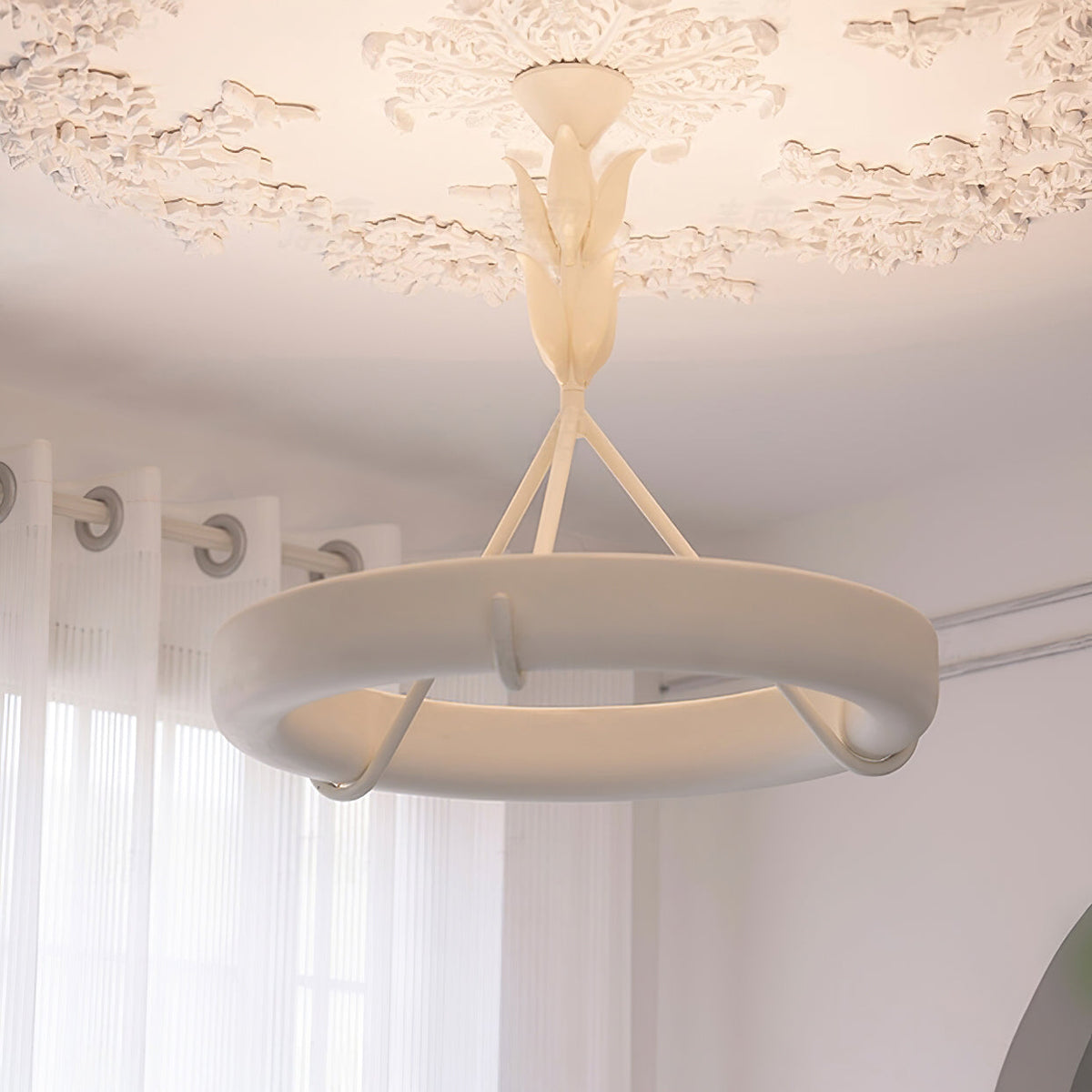 Near view of the lit plaster ring and three struts of this Clérachic ceiling light, with a leaf stem and a plaster rose above.