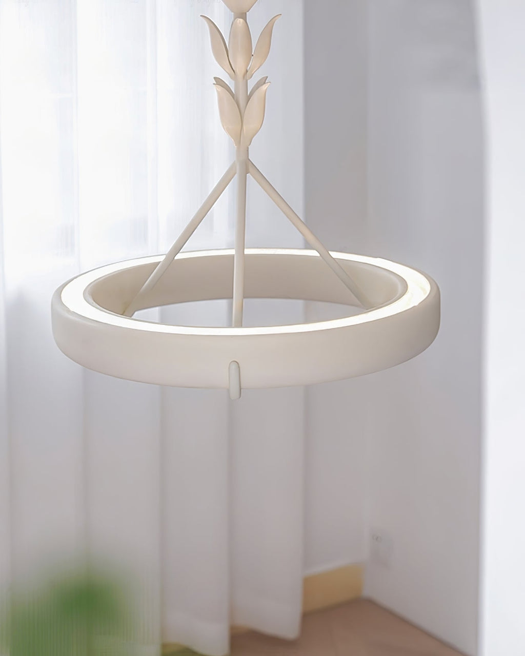 Lit Clérachic ceiling light seen close up, its plaster ring glowing along the inner edge, with sheer curtains behind.