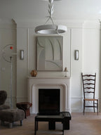 This Clérachic ceiling light seen from below in a tall room, above a white fireplace with a relief panel and a woolly stool.