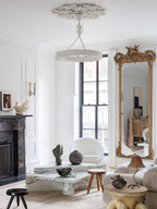 Clérachic ceiling light in a bright living room with a gilt mirror, a marble coffee table and a black fireplace.