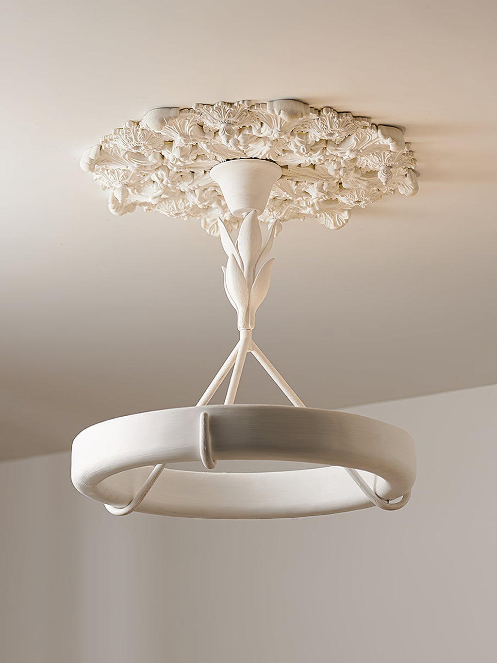 Looking up at the plaster ring, three struts and rose of this Clérachic ceiling light, with a plain wall in the background.