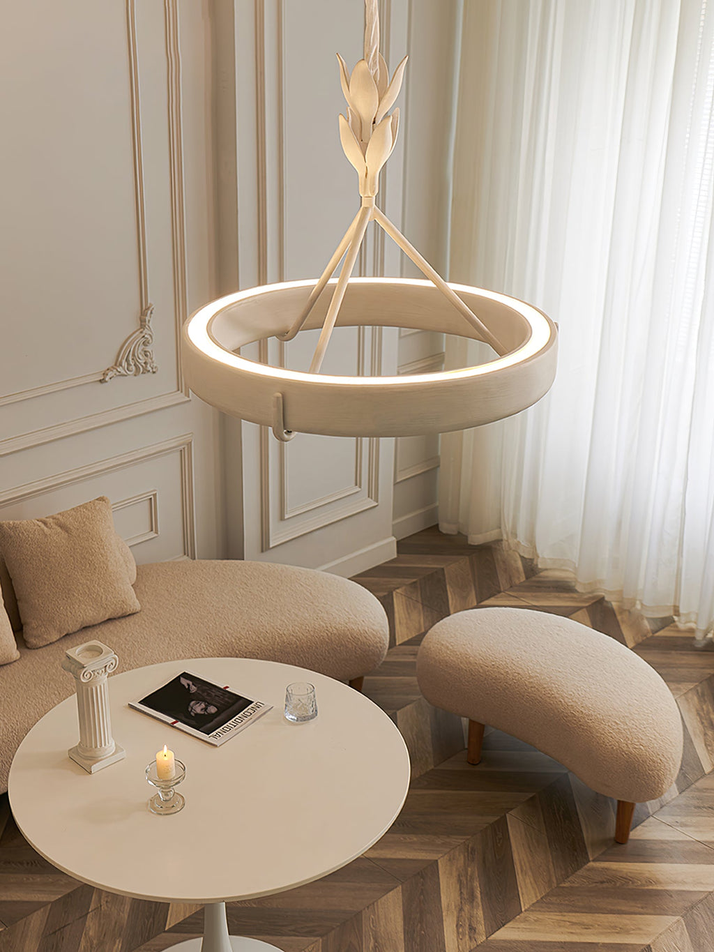 Glowing Clérachic ceiling light over a low round table and two soft beige seats, on a herringbone floor in a panelled room.