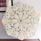 Detail of the carved plaster ceiling rose from Clérachic, its acanthus leaves and flowers in white relief, held up against a wall.