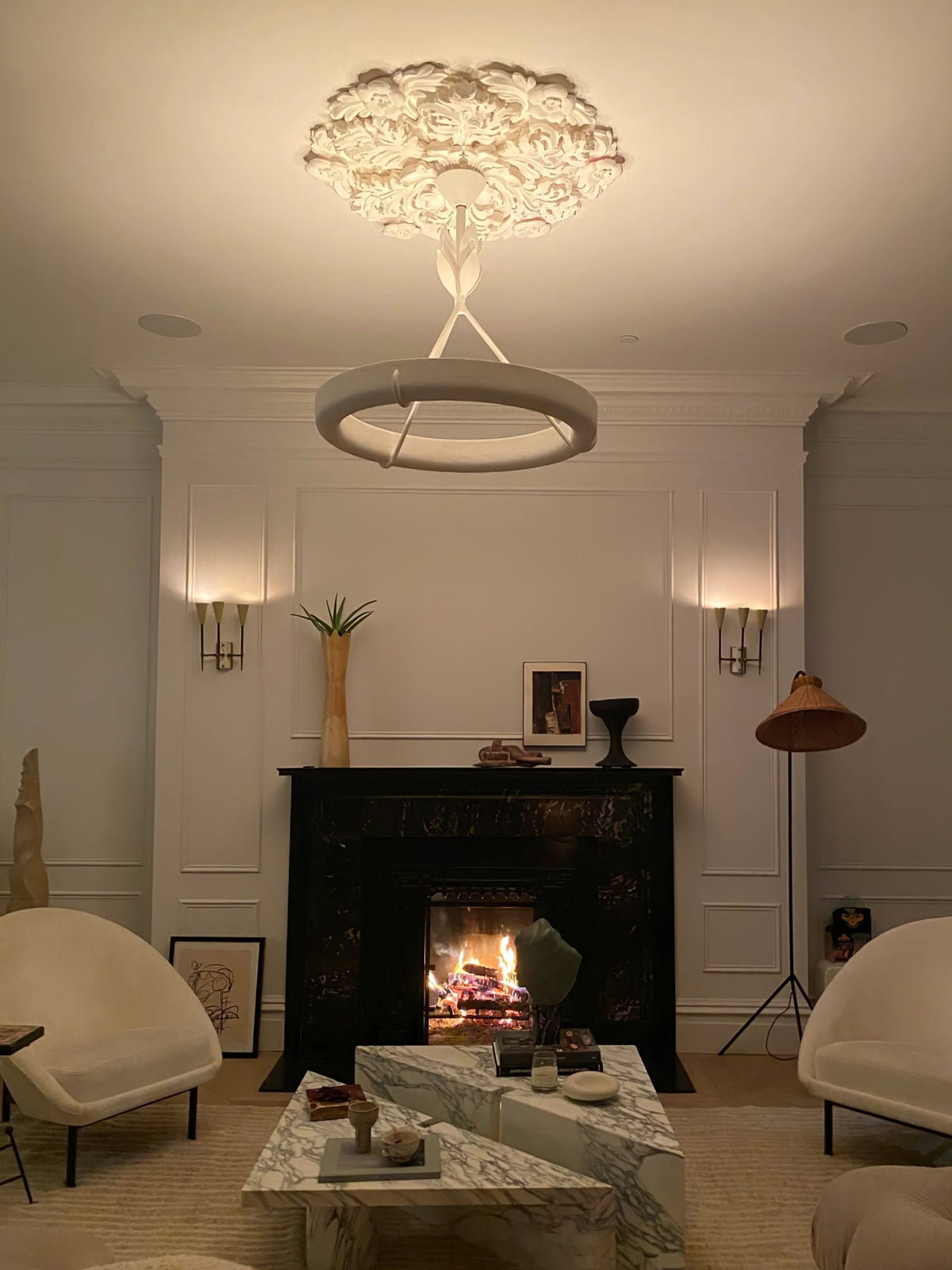 Lit Clérachic ceiling light under a plaster rose in the evening, with a fire burning in the fireplace below it.