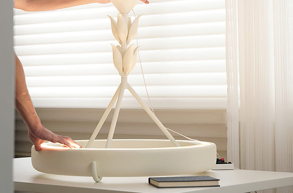A hand rests on the plaster ring of this Clérachic ceiling light as it stands on a white table before sheer blinds.