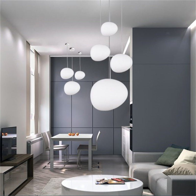 Cluster of Clérachic white glass pebble pendants over a dining table in a modern grey kitchen and living space.