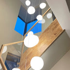 Looking up a timber staircase with a glass balustrade, past a column of Clérachic white glass pebble pendants.