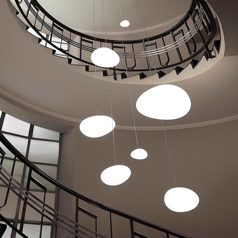 Clérachic white pebble pendants hang at different heights through a spiral stairwell with a black metal balustrade.