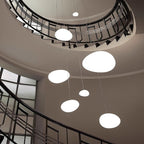 Clérachic white pebble pendants hang at different heights through a spiral stairwell with a black metal balustrade.