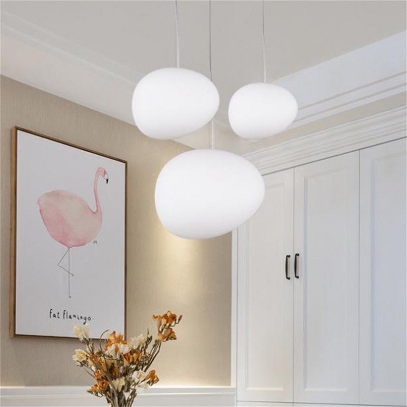 Three white Clérachic pebble pendants hang in a dining room beside a framed flamingo print and white panelled cupboards.