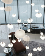 Clérachic pebble pendants in assorted sizes hang in a bright lobby over a brown chaise and a marble floor.