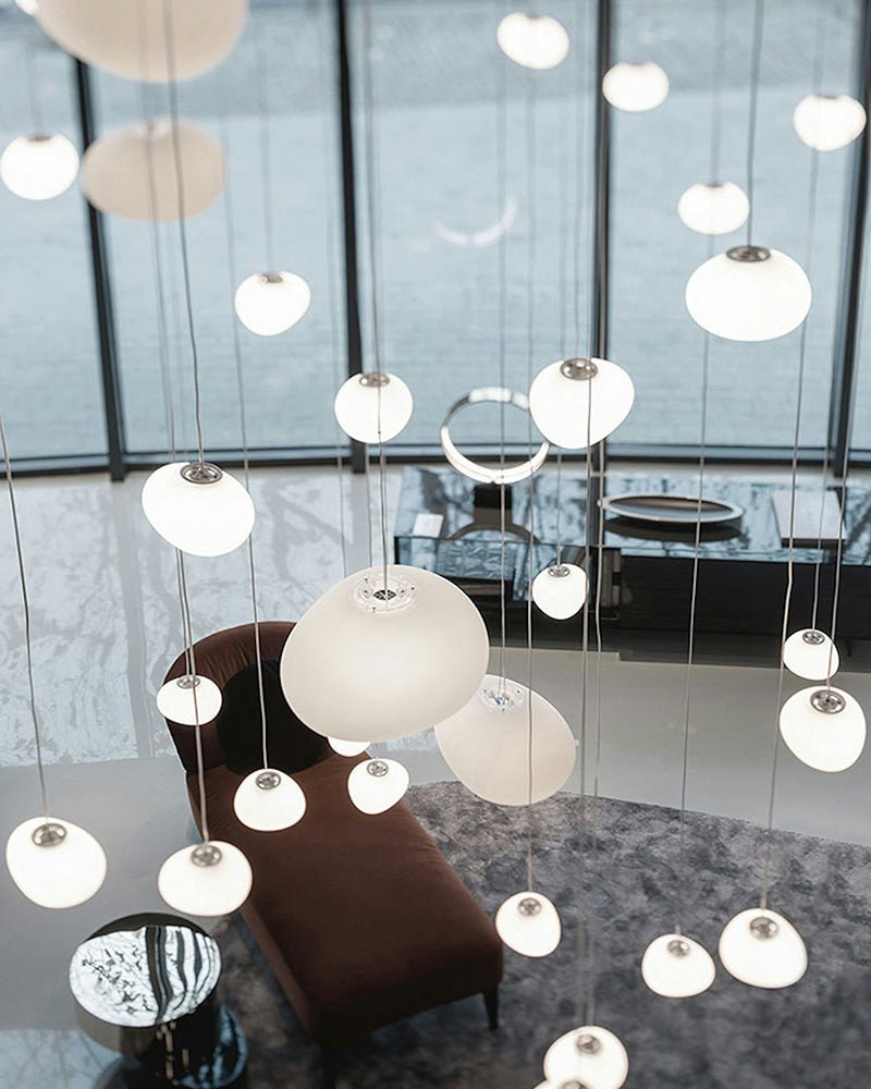 Clérachic pebble pendants in assorted sizes hang in a bright lobby over a brown chaise and a marble floor.
