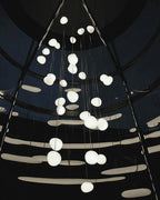 Dozens of Clérachic pebble pendants glow against a dark domed ceiling with curved light bands.