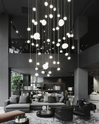 A tall cascade of small Clérachic glass pebble pendants hangs over a dark grey lounge with sofas and armchairs.