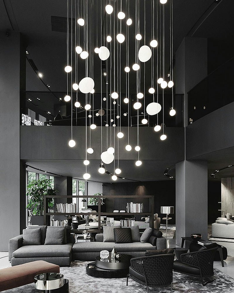 A tall cascade of small Clérachic glass pebble pendants hangs over a dark grey lounge with sofas and armchairs.