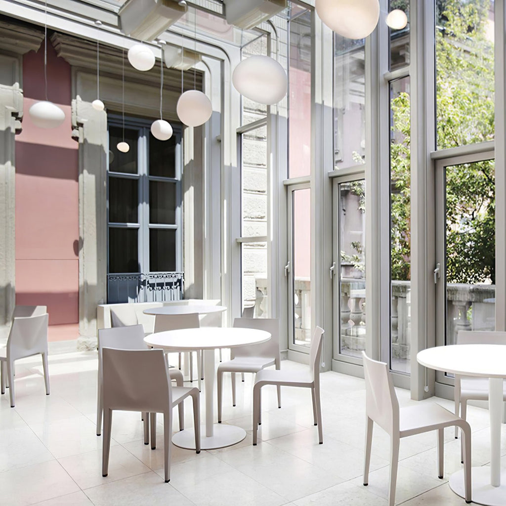 Clérachic pebble pendants hang high in a pale café with tall windows, white round tables and moulded chairs.