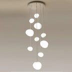 Cluster of nine Clérachic white glass pebble pendants hanging at staggered heights from one round ceiling canopy.