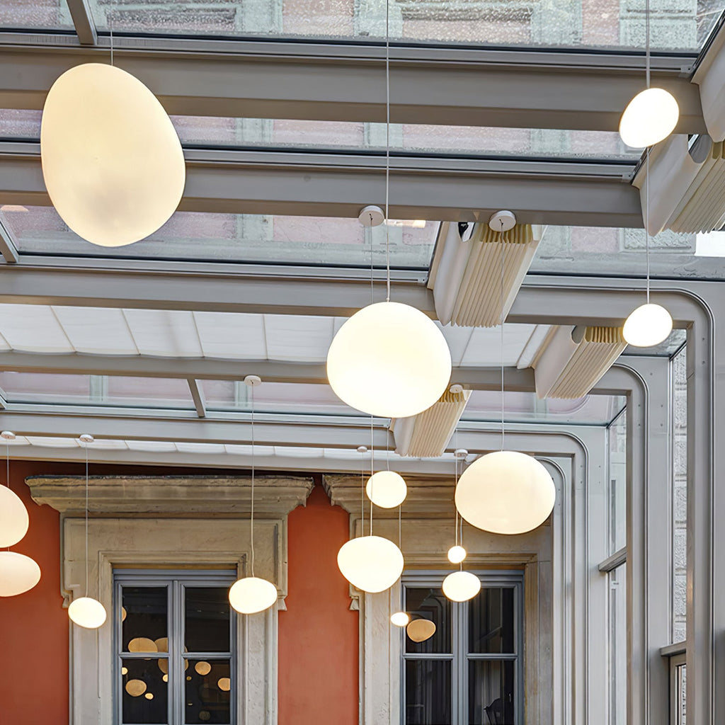 Clérachic pebble pendants glow warm beneath a glazed roof, with an orange wall and stone-framed windows behind.