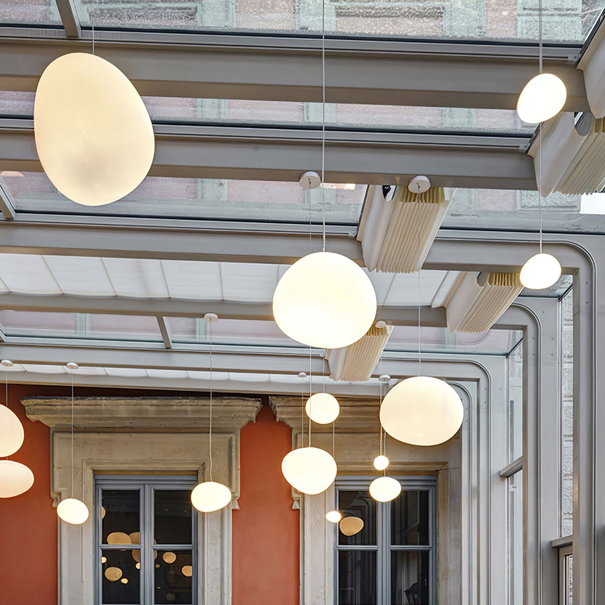 Clérachic pebble pendants glow warm beneath a glazed roof, with an orange wall and stone-framed windows behind.