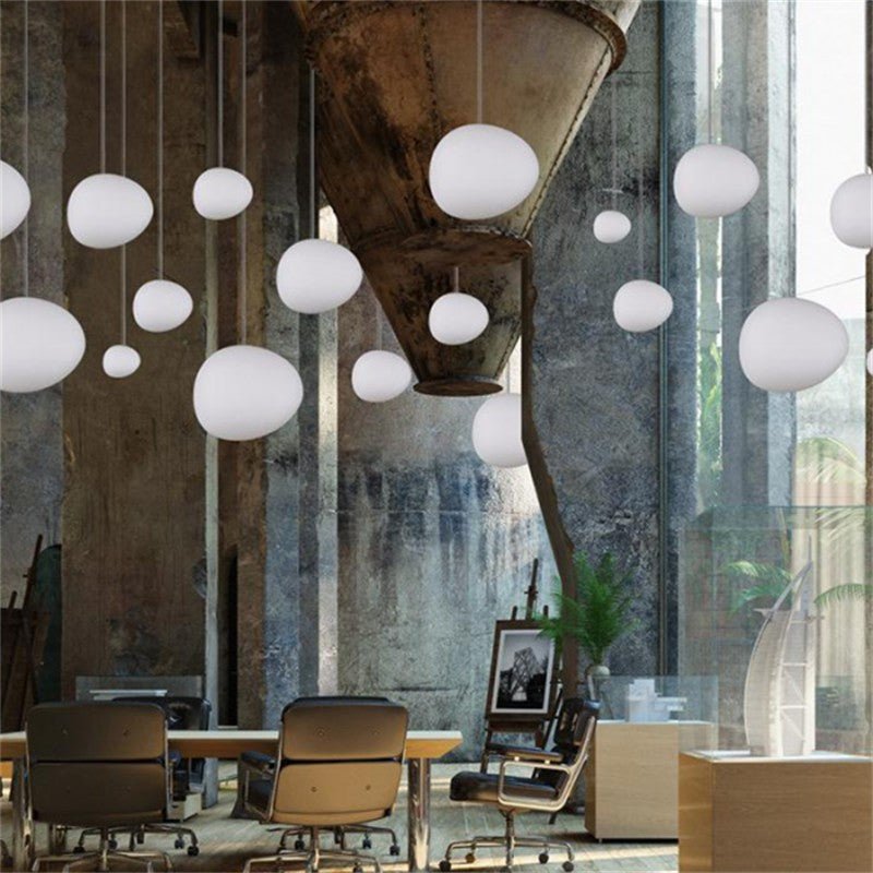 Clérachic white glass pebble pendants hang in a high loft in front of a weathered concrete wall.