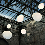 Clérachic white pebble pendants hang beneath a steel-framed glass roof, with a weathered brick wall behind.
