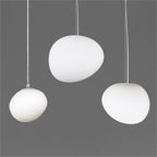 Three white satin glass pebble pendants from Clérachic in different sizes, on a mid-grey background.