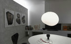 A single Clérachic white glass pebble pendant above a white oval table, with three framed prints on the wall.