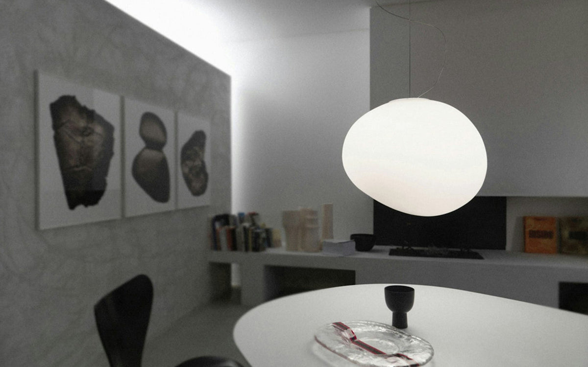 A single Clérachic white glass pebble pendant above a white oval table, with three framed prints on the wall.