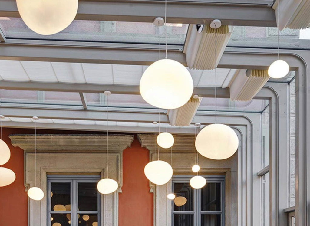 Wide shot of Clérachic pebble pendants under a glass roof, with the warm light catching the satin glass.