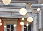 Wide shot of Clérachic pebble pendants under a glass roof, with the warm light catching the satin glass.