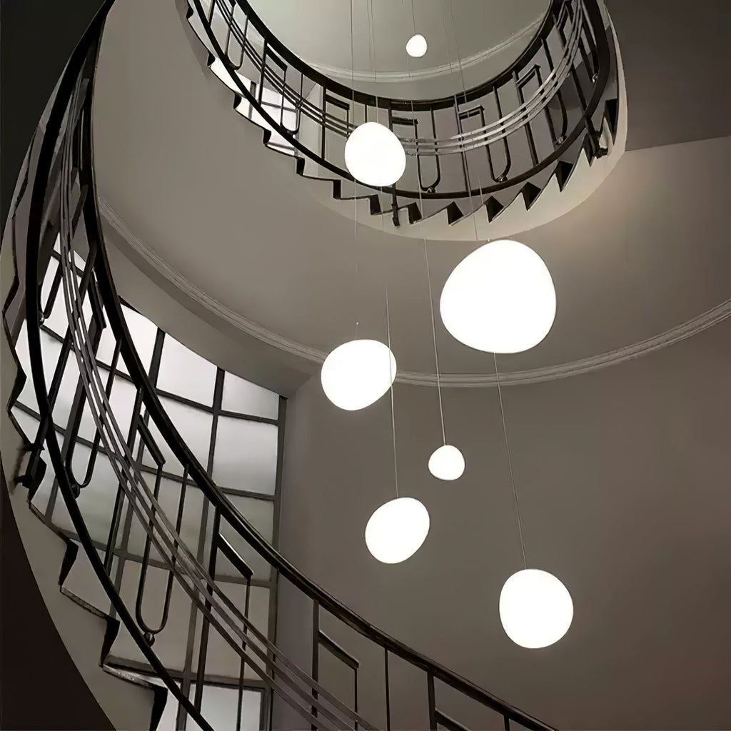 Seven Clérachic white pebble pendants hang down the centre of a spiral staircase with a black iron balustrade.
