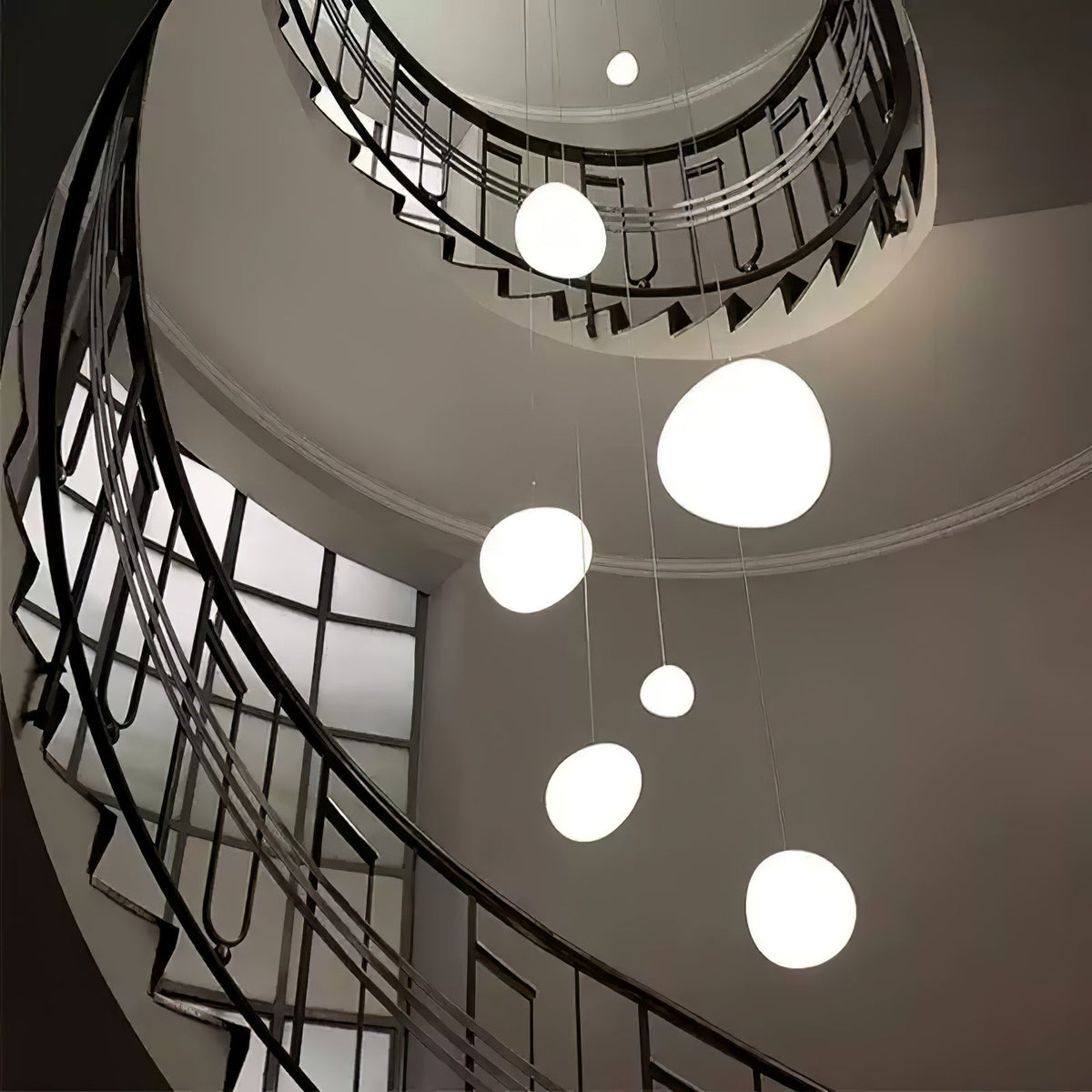 Seven Clérachic white pebble pendants hang down the centre of a spiral staircase with a black iron balustrade.