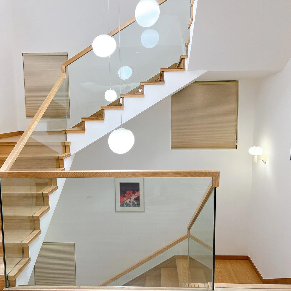 Clérachic white glass pebble pendants rise past a light oak staircase with glass panels and a framed print.